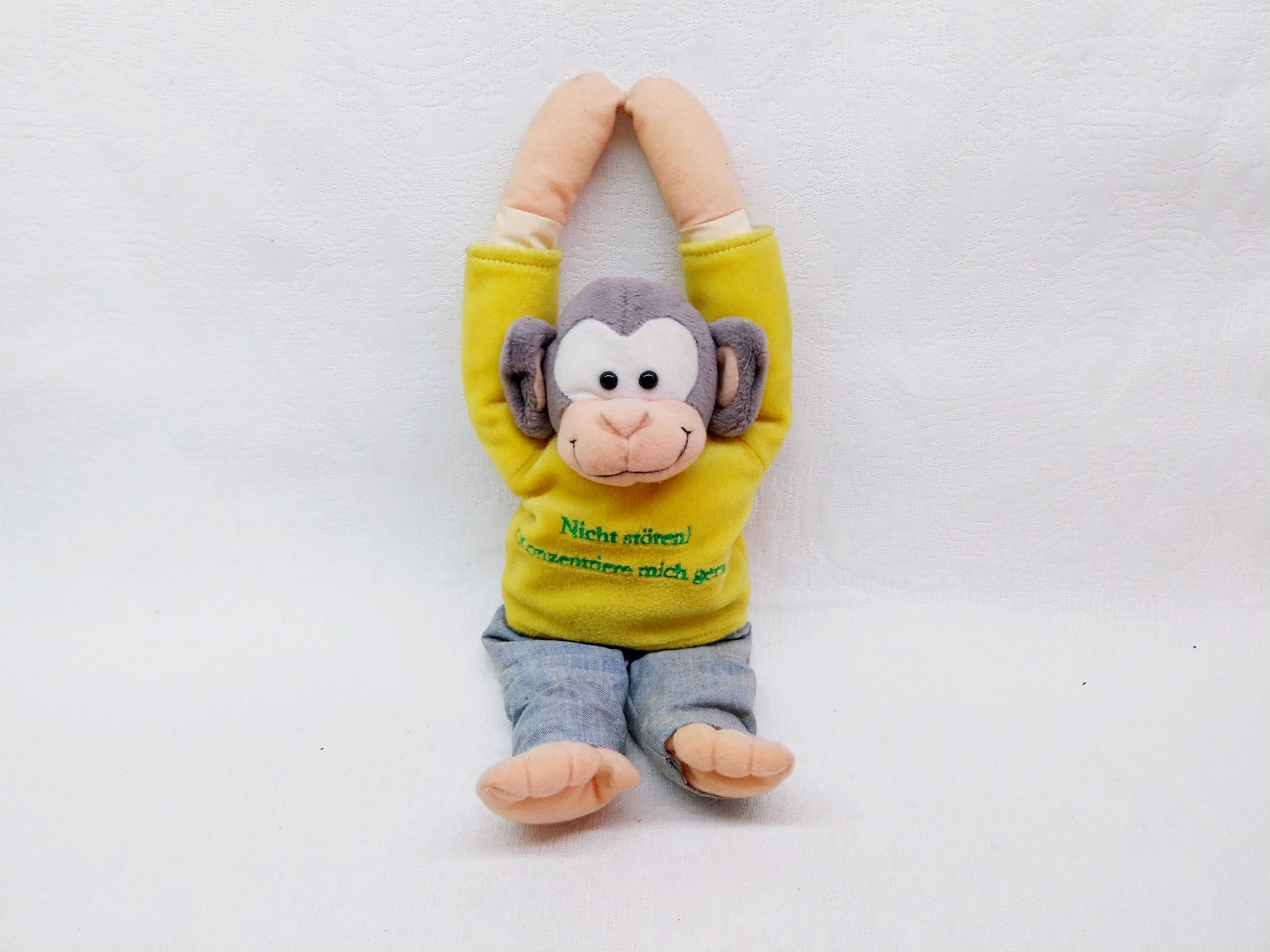 Plush monkey toy in yellow shirt and jeans with arms raised