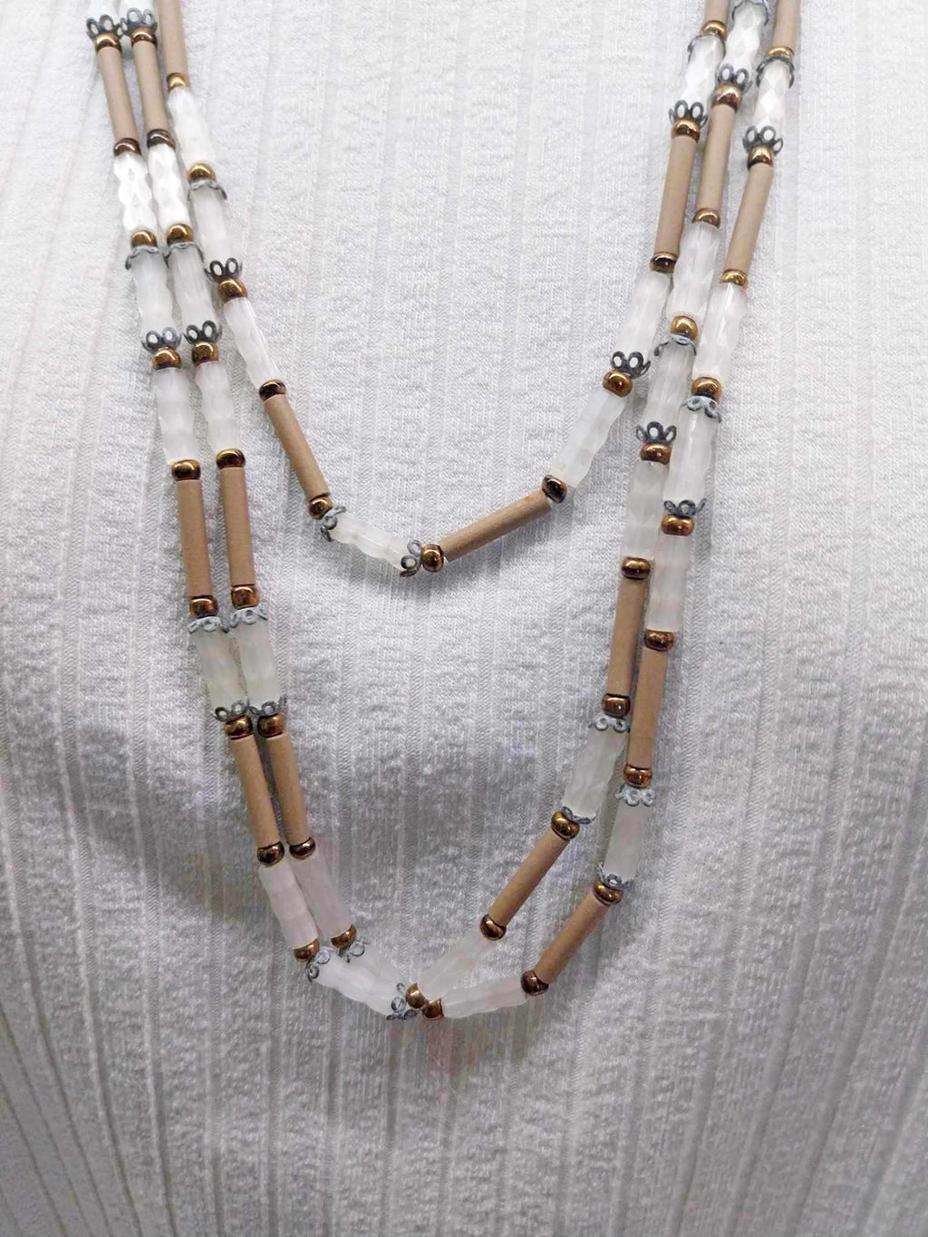 Vintage multi-strand white and beige glass tube necklace laid flat on white fabric