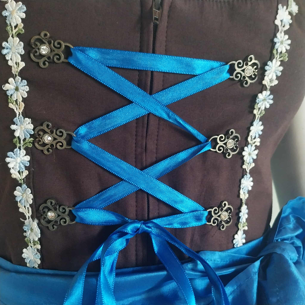 Close-up of Stockerpoint dirndl bodice detail — blue satin cross-lace ribbon with bronze rhinestone clasps and floral trim
