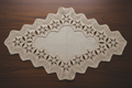 Vintage hand-crocheted oval linen doily with wide ecru lace border, top-down view on dark walnut table