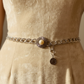 Close-up of vintage silver chain belt with sunburst pearl brooch and coin pendant worn at waist