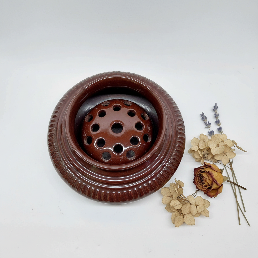 Top-down view of vintage dark brown glazed ceramic flower frog showing perforated holes, with dried flowers beside it