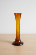 Vintage amber glass bud vase with twisted spiral neck on light wooden table, cream background