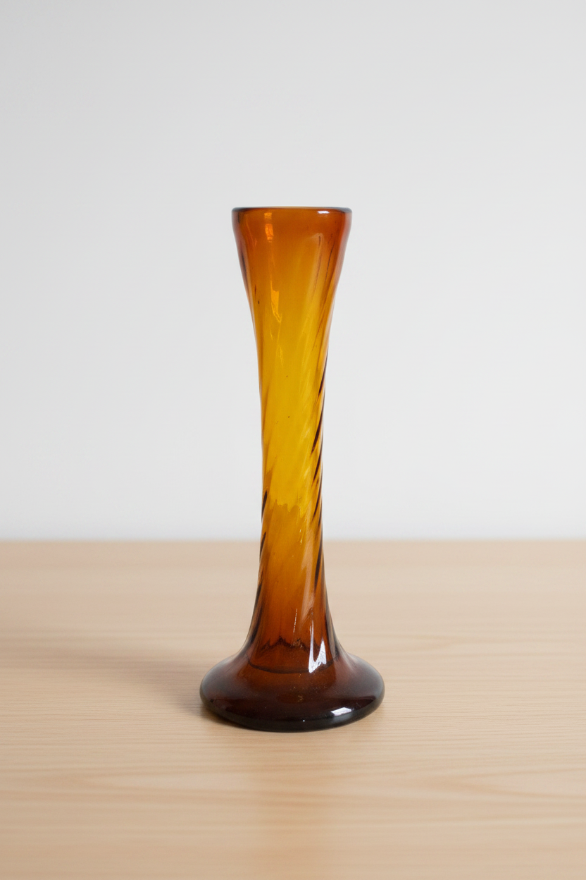 Vintage amber glass bud vase with twisted spiral neck on light wooden table, cream background