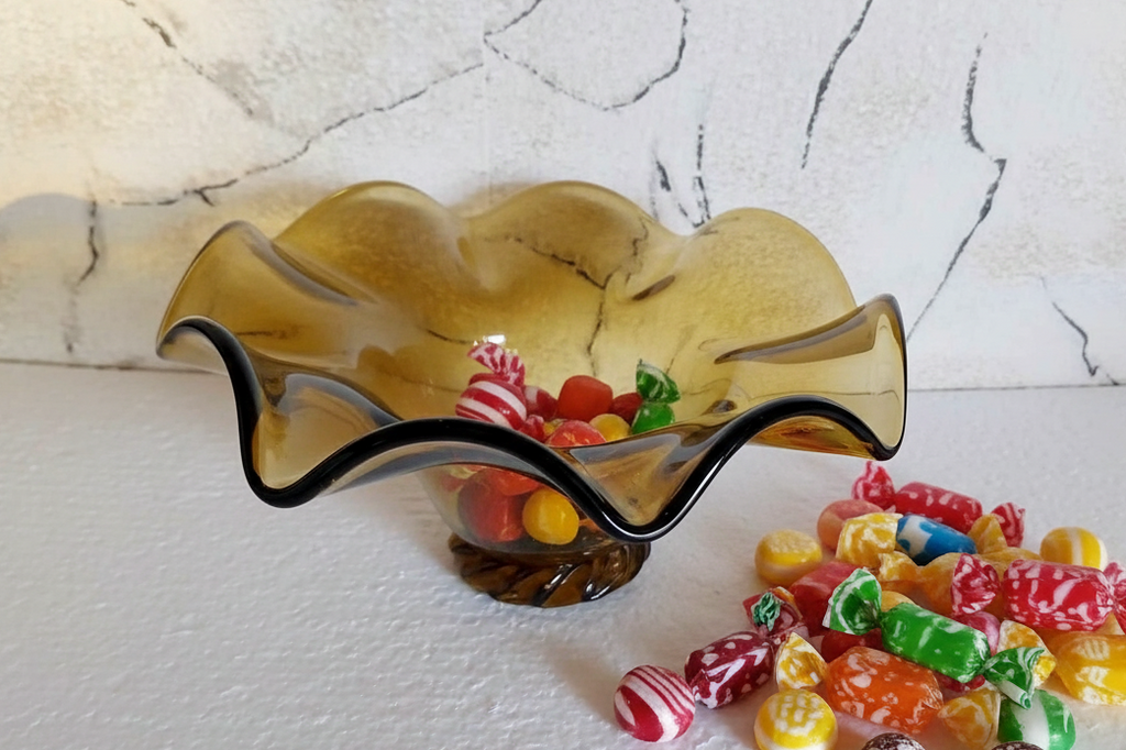 Vintage amber glass candy bowl with ruffled rim, colorful candies inside and beside it on white background