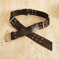 Vintage black leather belt with double buckle and silver eyelets on light wooden surface