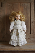 Vintage porcelain doll with curly blonde hair and lace dress in vintage setting