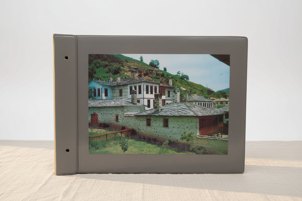 Vintage photo album with grey cardboard cover and Balkan village scene on cream linen background
