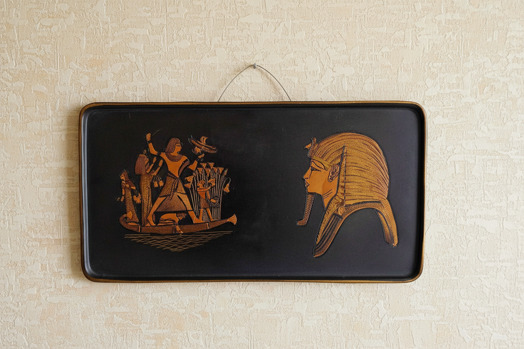 Vintage Egyptian wall plaque with Tutankhamun mask and pharaoh on Nile, hanging on light beige wall, bright natural light